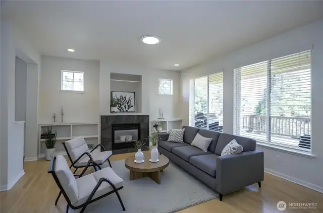 Bright and welcoming living area with convenient built-in shelving, expansive windows that fill the space with natural light, and a cozy gas fireplace for added warmth and comfort - virtually staged.