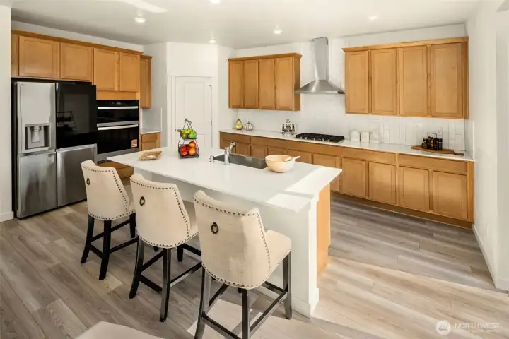 Beautifully finished kitchen featuring a breakfast bar at the center island, stainless steel refrigerator, wall ovens, dishwasher, and lots of cabinet space!