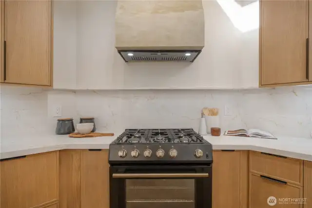 New gas range with venetian plaster hood vent. Spice and sheet pan pull outs flank the range.