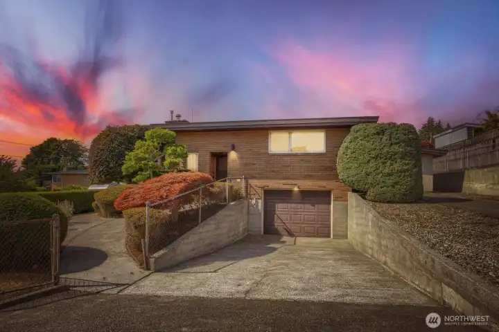 Striking Mid-Century Exterior This beautifully maintained mid-century home showcases timeless design with its clean lines, brick façade, and expansive windows that capture natural light. The elevated setting and landscaped approach create a welcoming presence, complemented by mature shrubs and manicured hedges. A private driveway leads to the attached garage, while the sunset backdrop enhances the home’s warm, inviting appeal. Striking Mid-Century Exterior This beautifully maintained mid-century home showcases timeless design with its clean lines, brick façade, and expansive windows that capture natural light. The elevated setting and landscaped approach create a welcoming presence, complemented by mature shrubs and manicured hedges. A private driveway leads to the attached garage, while the sunset backdrop enhances the home’s warm, inviting appeal.