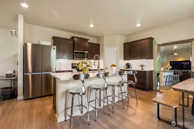 This modern kitchen is a chef's dream, featuring sleek stainless steel appliances, beautiful dark wood cabinetry, and a large center island perfect for casual dining or entertaining. The bright quartz countertops add a touch of elegance and offer ample workspace for meal prep, while the stylish subway tile backsplash completes the contemporary design. With plenty of storage and an open concept that flows seamlessly into the dining and living areas, this kitchen is designed for both functionality and style. Whether you're hosting guests or enjoying a quiet meal at the breakfast bar, this space is sure to impress!