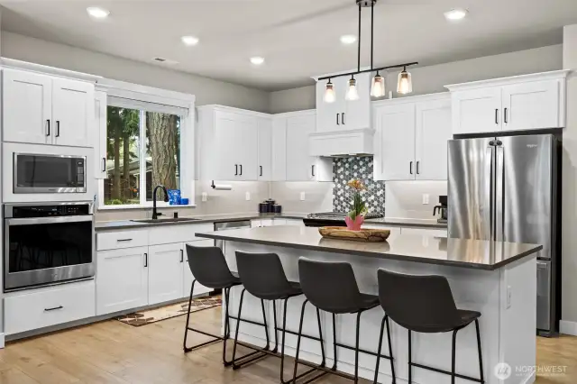Gourmet kitchen features large island, double ovens, undercabinet lighting, white cabinetry, soft close cabinetry, black fixtures and handles as well as black faucet and black undermount single basin sink.