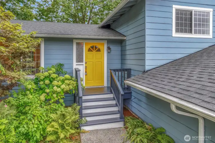 Approaching the entryway, the front steps lead to a covered landing surrounded by vibrant plantings. This welcoming entrance creates a warm first impression for guests.