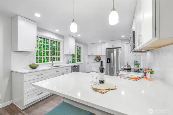 A closer view of the kitchen reveals an expansive island with seating, ideal for casual dining or conversation while cooking. The bright finishes and pendant lighting add a polished touch.