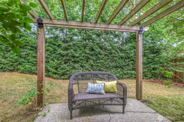 A charming pergola-covered patio creates a quiet garden retreat. This private nook is perfect for reading, relaxing, or enjoying the surrounding greenery.