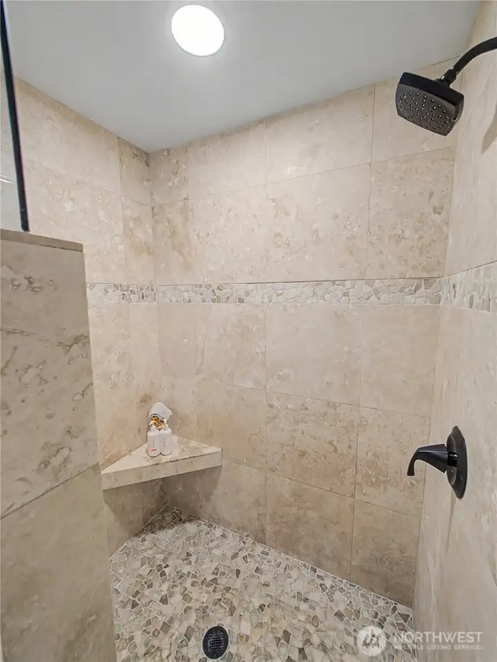 The beautifully updated walk-in shower features natural stone tile, a pebble-style floor, and elegant finishes that create a spa-like retreat. Thoughtfully designed with timeless materials, this space offers both luxury and comfort.