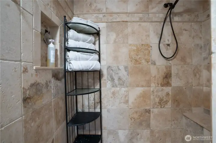 Natural stone walk in shower with three shower heads, shelves, and a bench. This is your own personal spa