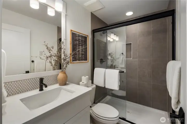 Lower-Level Bathroom: Sleek full bathroom with modern finishes, a frameless glass shower, and designer tile accents. Perfectly situated to serve the lower-level suite or bonus space, it adds functionality and privacy for everyday living or overnight guests.    Photos are from a previous Glacier model home at Foxmoore and are for visualization purposes only - colors, selections, and included feature can and will vary.