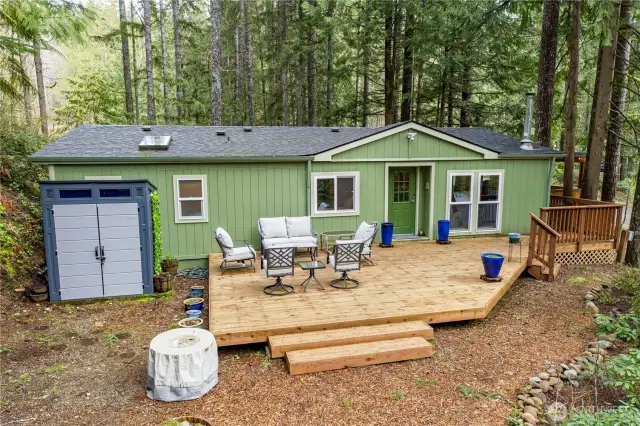 This angled view highlights the freshly updated deck and the inviting outdoor seating area—ideal for lounging, dining, or enjoying the surrounding forest.