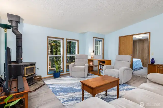 Cozy up in the living room beside the wood-burning stove, perfect for chilly evenings. Large windows invite in natural light and forest views, creating a peaceful, nature-inspired atmosphere.