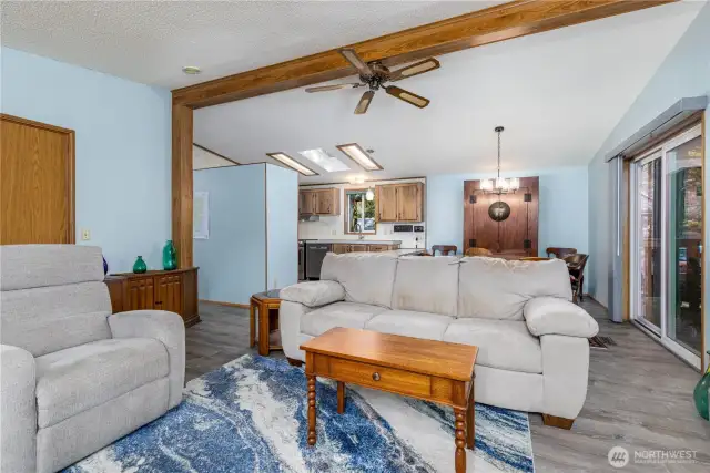 This open-concept living space blends comfort and functionality with vaulted ceilings, wood accents, and abundant natural light. The layout seamlessly connects the living room, dining area, and kitchen, creating an inviting environment for entertaining or quiet evenings at home. Sliding glass doors open to the covered deck, seamlessly transitioning from the living space into the outdoors.
