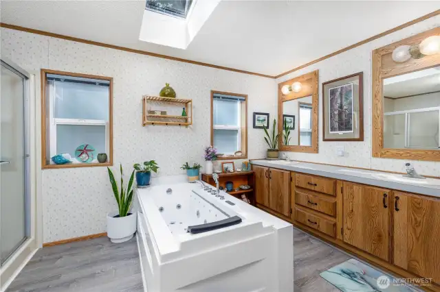 This spacious bathroom is filled with natural light from a skylight above, creating a bright and welcoming atmosphere. The jetted soaking tub is the centerpiece, perfect for relaxing after a day of adventure. Dual sinks and ample storage make the space practical for everyday living or hosting guests. Updated flooring adds a fresh, modern touch while still keeping a cozy cabin feel