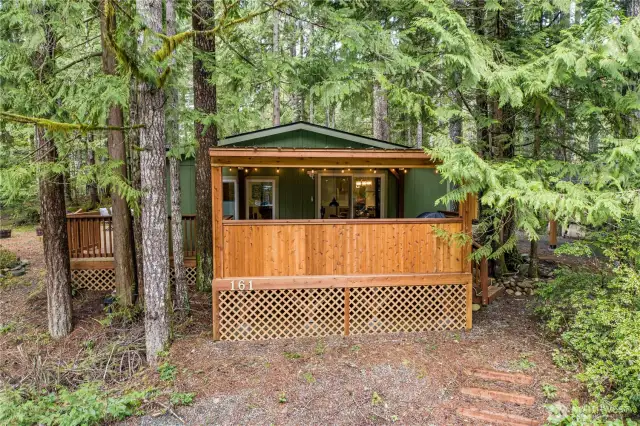 Tucked into the trees, this inviting woodland retreat features a charming front entry with privacy lattice and natural stone steps leading up from a serene garden bench area. Surrounded by lush forest and moss-covered landscaping