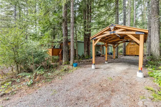 covered parking surrounded by the natural beauty of the Pacific Northwest. The gravel driveway provides additional parking space, while the nearby powered shed offers extra storage or workshop potential