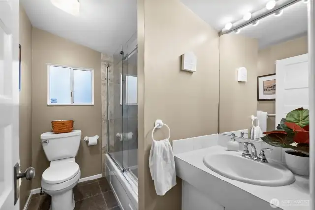 The main-level full bathroom offers sleek glass shower doors and a soothing tub, ideal for unwinding and soaking away your troubles on a chilly, rainy evening.