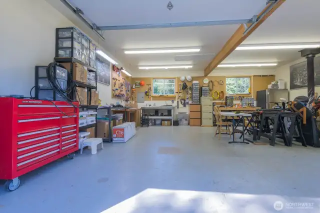 Interior of workshop, with an extra bay for boat or 3rd vehicle. Well lit area with a wood stove. Electrical panel is on the back wall.
