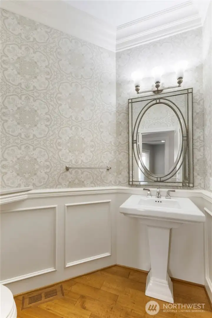 The guest bathroom features a pedestal sink, wood flooring, wainscoting and more.