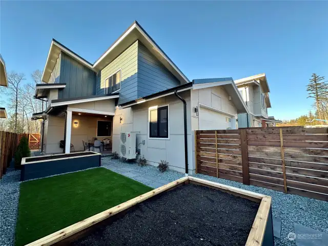 View of the fenced back yard featuring turf lawn, and raised bed planters and gate access to the alley.