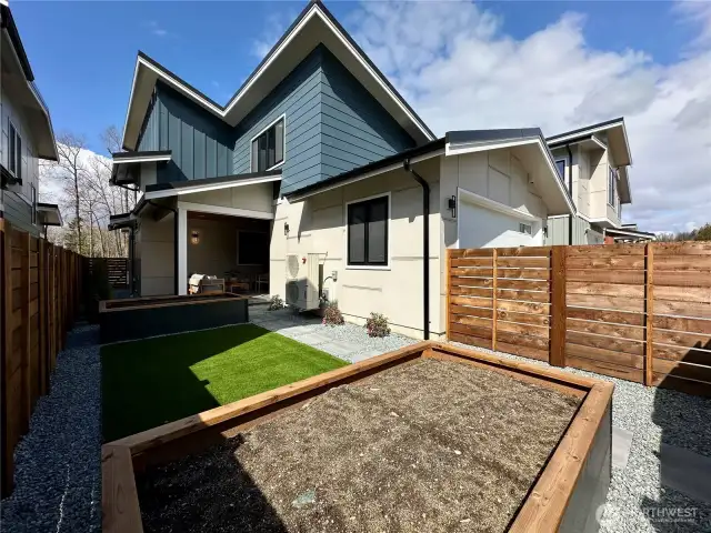 View of the fenced back yard featuring turf lawn, and raised bed planters and gate access to the alley.