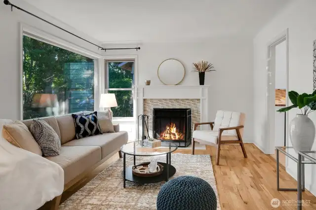 another view of the living room with large picture windows overlooking the front yard and the entryway to the right leading to the kitchen