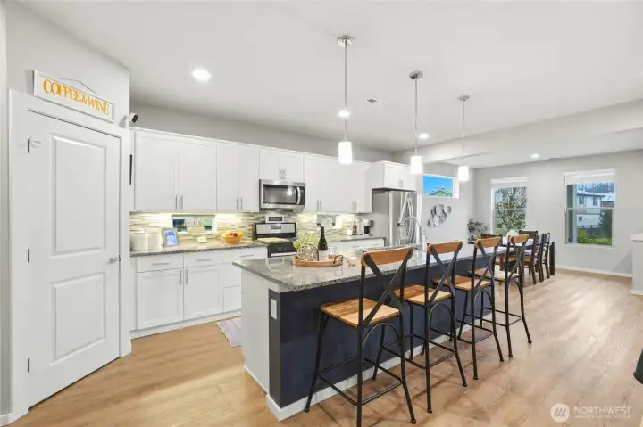 Large modern kitchen featuring granite countertops, oversized island seating, stainless appliances, and ample cabinet storage designed for entertaining.