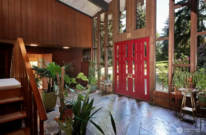 Grand atrium with south facing wall of windows. There is a bedroom and a guest room on either side of the atrium. Stairs to the upper level Primary Suites is glimpsed along the left edge of this photo.