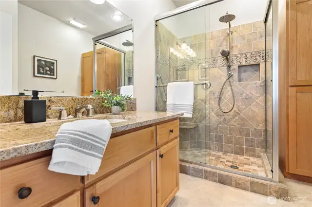 Tastefully updated bath suite with full tile shower, granite counters, extra cabinetry, and tile floors.