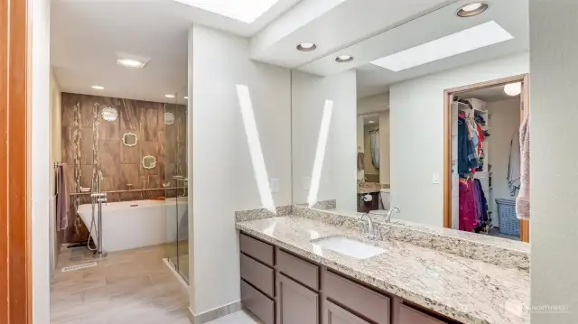 Fully remodeled spa-like primary en suite with tile floors, granite counters, large soaking tub, walk-in shower, two vanities, and large walk-in closet.