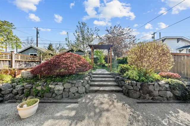 Charming stone steps and a pergola lead you through vibrant, terraced garden beds in this beautifully maintained outdoor oasis.