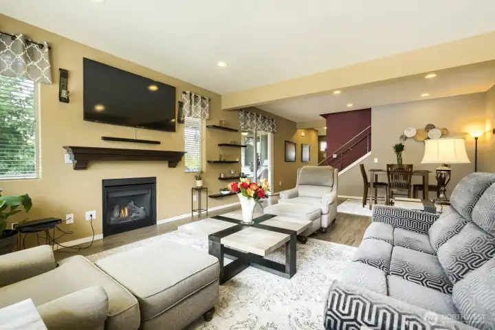 Expansive living room filled with natural light, featuring numerous windows, a cozy gas-burning fireplace, and an adjoining dining area perfect for entertaining.