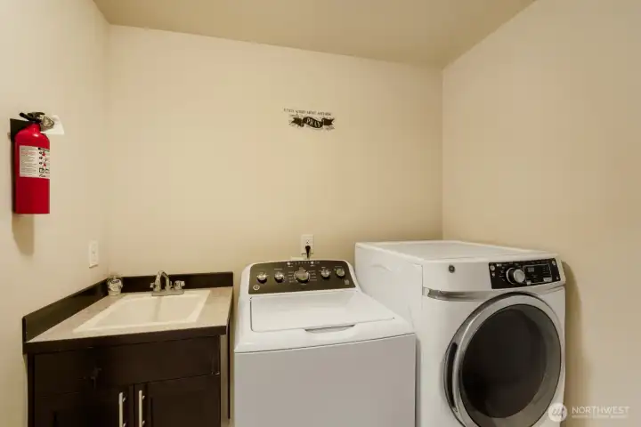 Generously sized laundry room equipped with a full-size washer and dryer, utility sink, and built-in cabinetry, plus extra space to add additional storage or custom cabinets if desired.