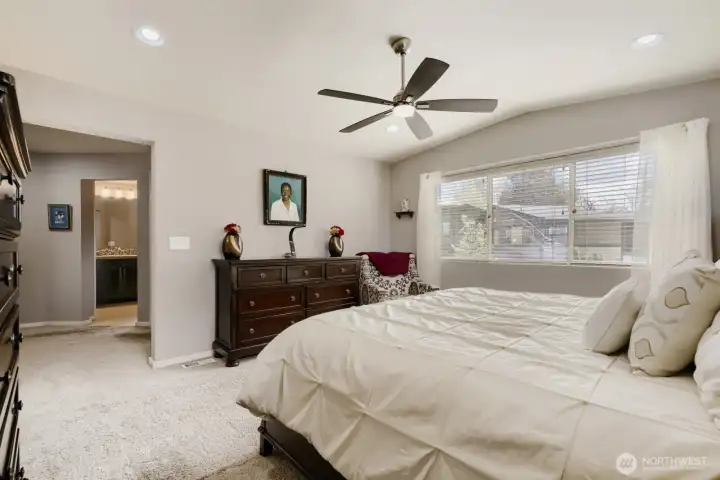 Gigantic primary suite featuring a luxurious 5-piece bathroom with dual sinks, soaking tub, separate shower, and a spacious walk-in closet, plus plush carpeting, ceiling fan, and a large window with blinds for natural light and comfort.