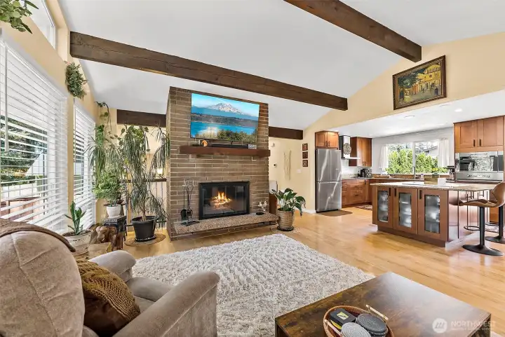 Gather and relax in the spacious family room featuring vaulted ceilings, striking wood beams, a charming wood-burning fireplace, expansive windows, and rich hardwood flooring