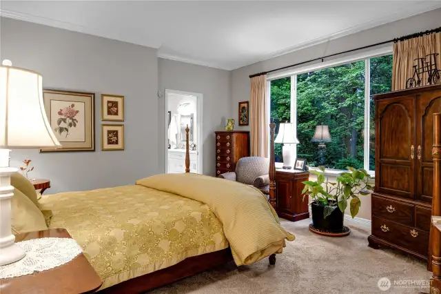Main level primary ensuite bedroom. Neutral carpet. Crown molding. Big picture window with views of forested park behind. Paneled Quaker pocket door to Primary bath.