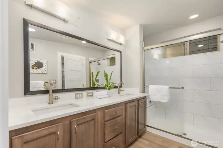 Clean-lined and calming, the ensuite bath features dual vanities, quartz counters, and an oversized glass shower wrapped in timeless large-format tile. Clean-lined and calming, the ensuite bath features dual vanities, quartz counters, and an oversized glass shower wrapped in timeless large-format tile.