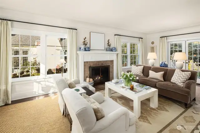 Light filled living room with walls of newer windows, wood burning fireplace and French doors to back deck and patio.