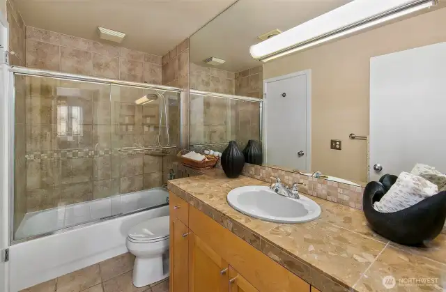 Spa like bath with marble counters, matching maple cabinets, and ceramic shower surround and tiled floors.