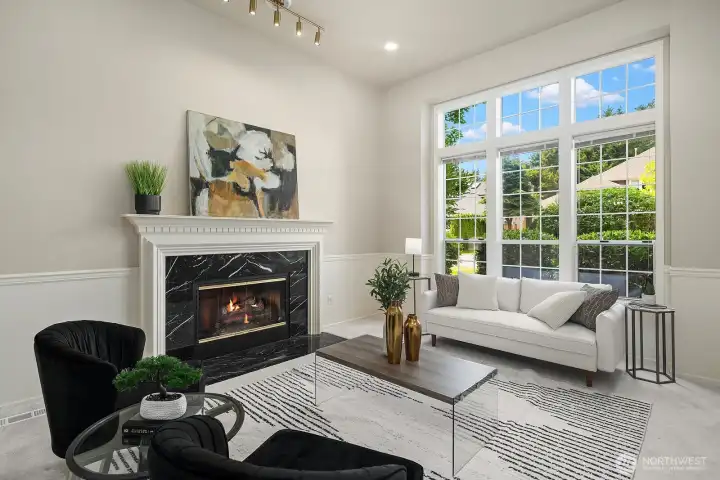 A closer look at the living room highlights the elegant fireplace surround, abundant natural light pouring in through large windows, and the lush greenery just beyond that brings a sense of calm to this beautifully appointed space.