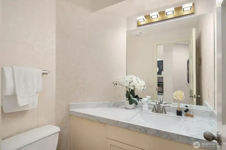 The main-level powder room features a warm vanity with ample counter space and bright lighting, offering guests a polished and convenient space just off the main living areas.