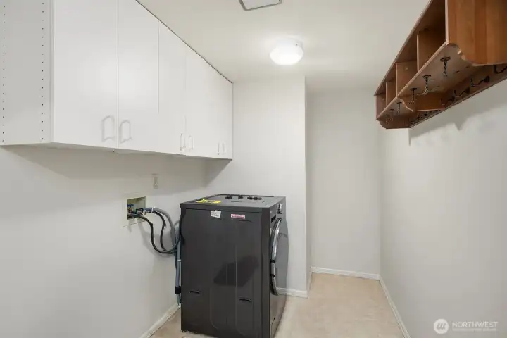 The dedicated laundry room features a full-size washer and dryer, abundant upper cabinetry for storage, and open shelving that keeps everything organized and easily accessible.