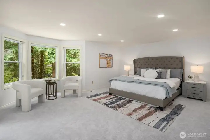 The expansive primary suite is a true retreat, with plush new carpeting, recessed lighting, and a wall of windows that bathe the space in natural light while framing the lush greenery just outside.
