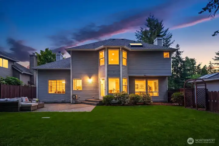 A stunning twilight view of the home showcases its warm, glowing interior and inviting outdoor spaces, with the lush backyard and classic Northwest architecture combining to create an unforgettable first and last impression.