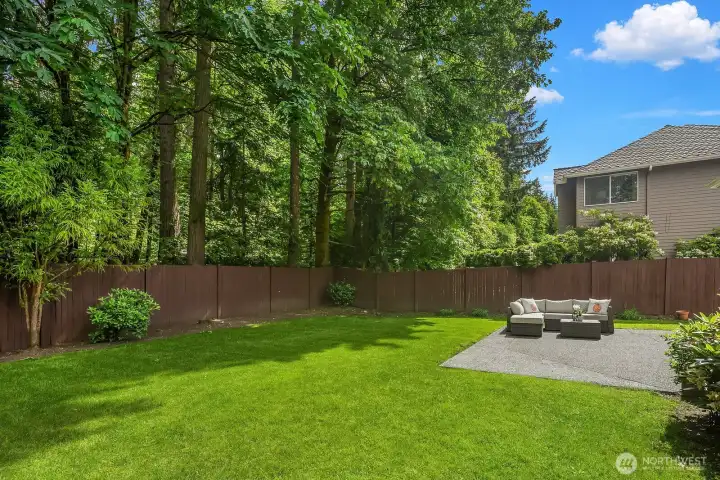 A lush, fully fenced backyard with a manicured lawn and mature trees along the greenbelt border creates an exceptionally private outdoor retreat that feels far removed from the bustle of everyday life.