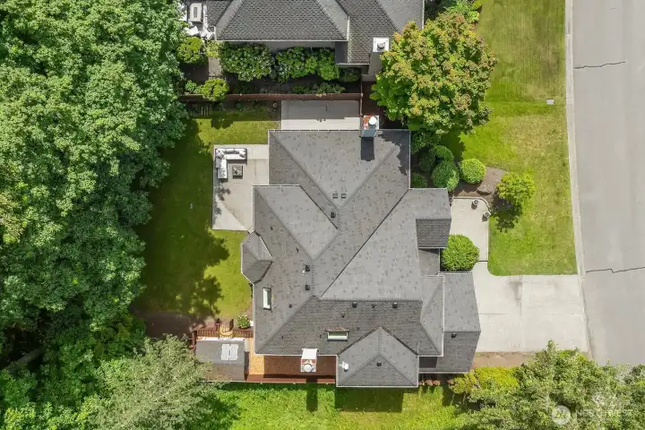 An aerial view reveals the home's generous footprint, well-maintained roofline, and prime positioning within the neighborhood, with mature trees and lush landscaping surrounding the property on all sides.