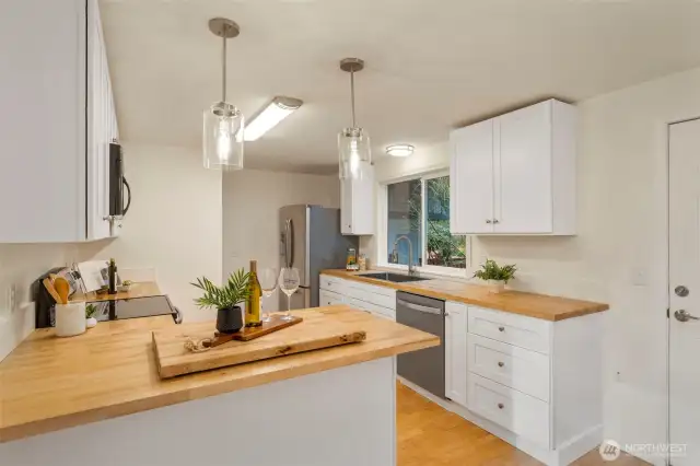 Inviting kitchen has butcher block counters, stainless appliances, and new white cabinets.