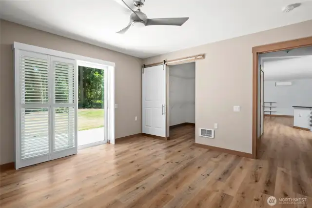 Primary bedroom with large walk in closet with a custom sliding barn door and glass slider with shutters to the back patio.