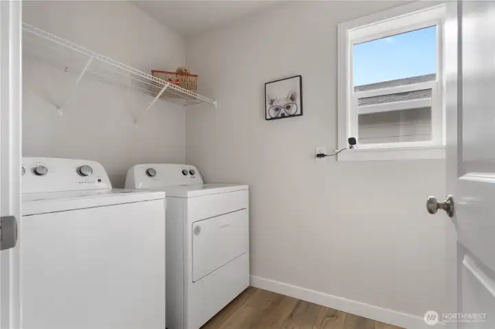 Upper-level laundry room with side-by-side washer/dryer and storage shelf.