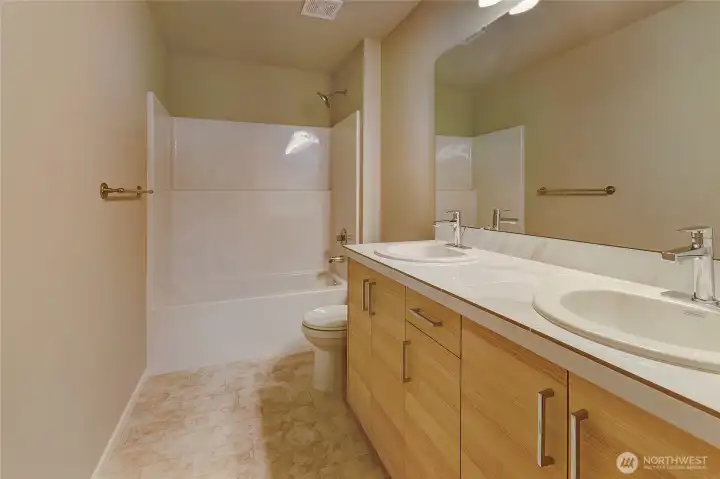 This expansive primary bathroom features a dual-sink vanity with a large mirror, a versatile tub-shower combo, and a spacious layout that enhances comfort and ease. With its clean design and thoughtful finishes, it offers a practical yet luxurious retreat within the home.