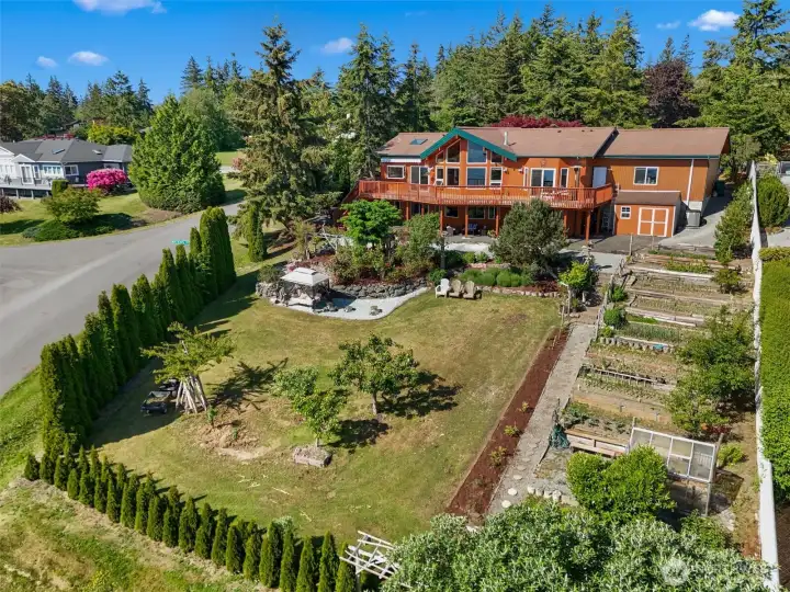 Aerial view showcasing the home, raised garden beds, greenhouse, and beautifully landscaped grounds.