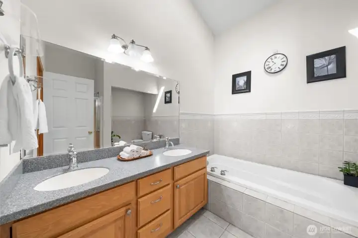 Spacious primary bath featuring dual vanities, a soaking tub, vaulted ceilings, and a skylight for abundant natural light